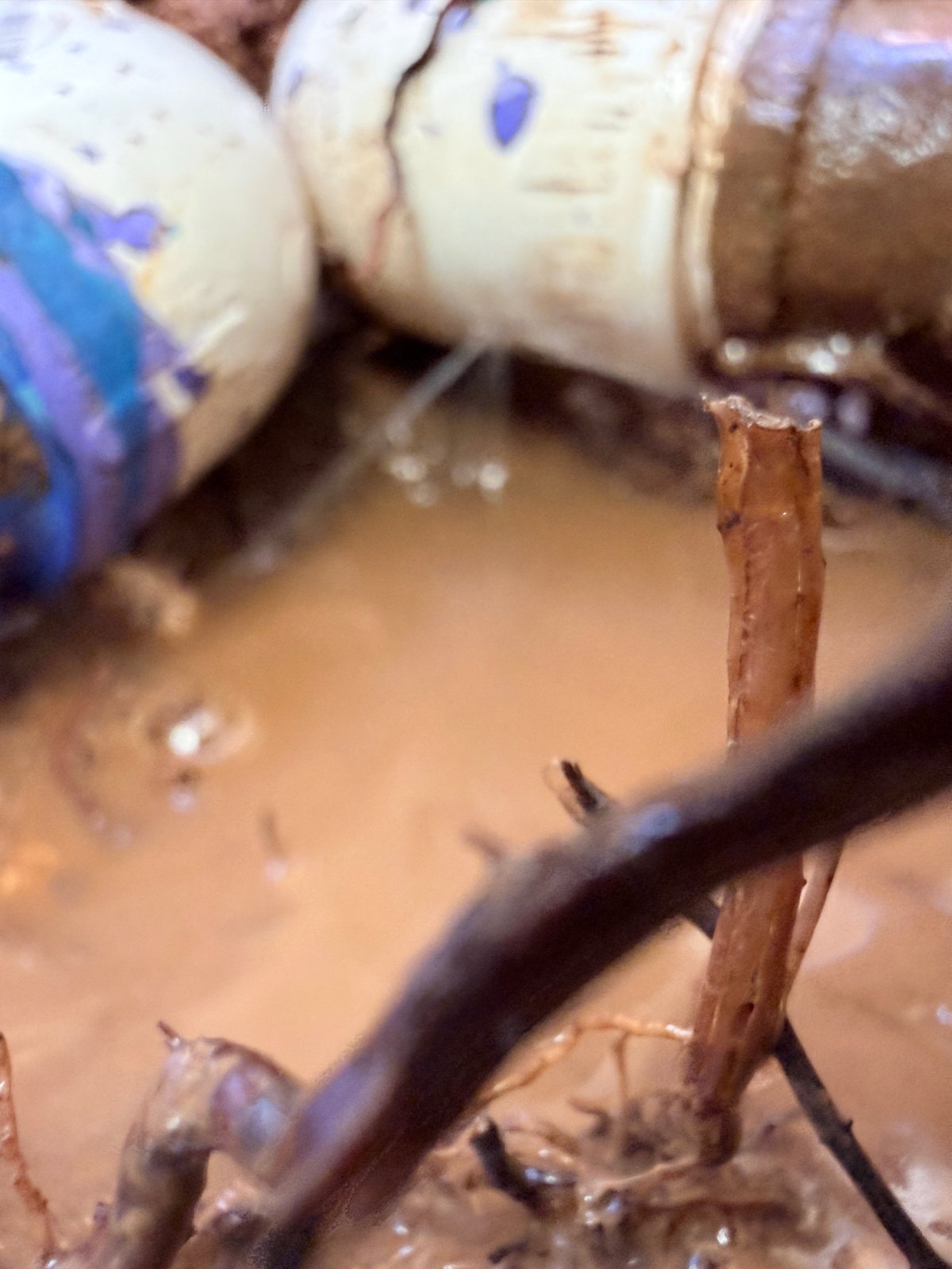Documented fractured PVC pipe with water spraying in an excavated work area.