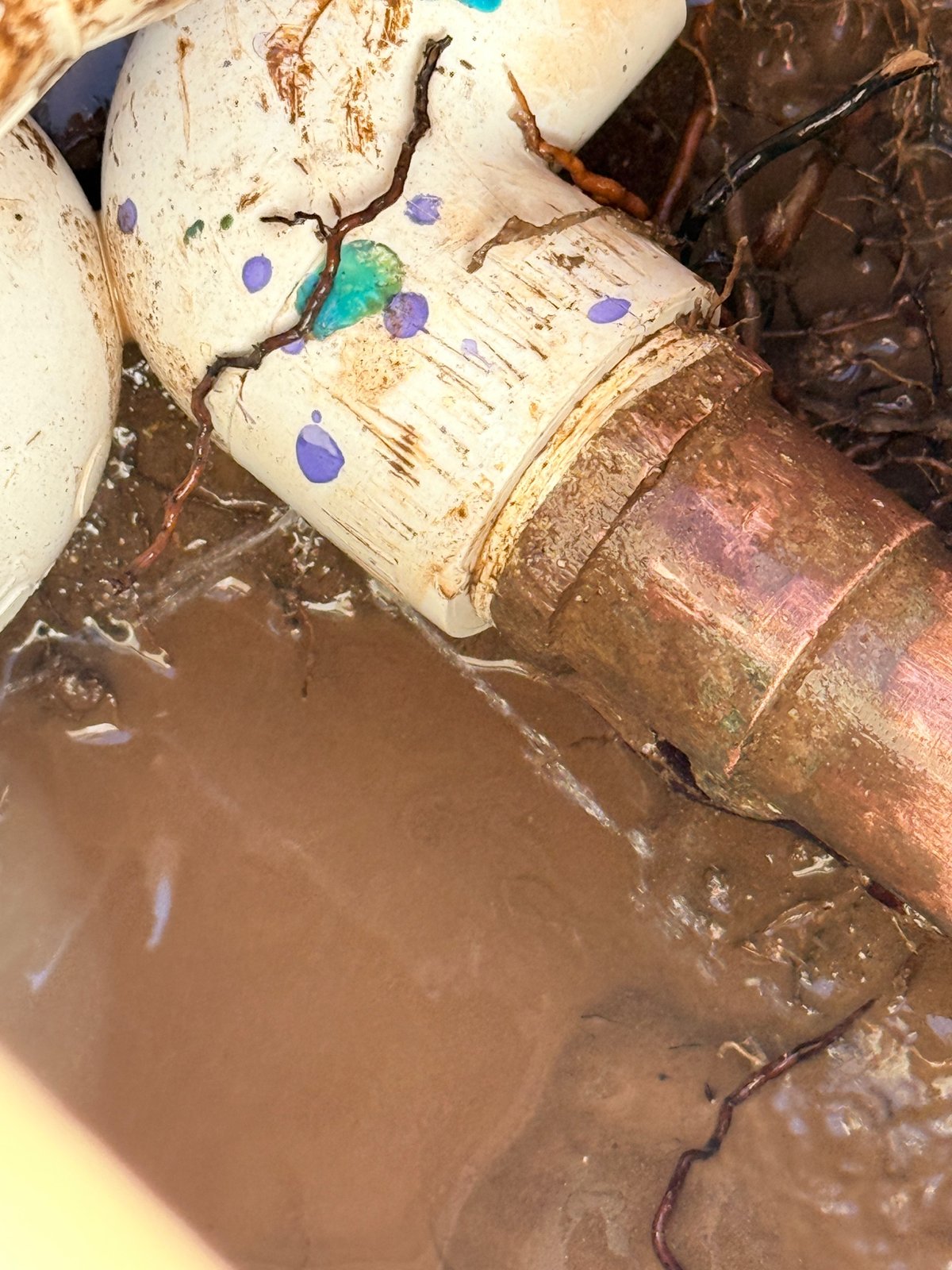Documented PVC-to-copper pipe connection with visible water leakage in an excavated work area.