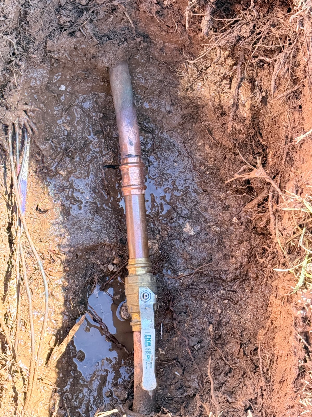 Documented copper water-line repair with a press-fit coupling and brass shut-off valve in an excavated trench.